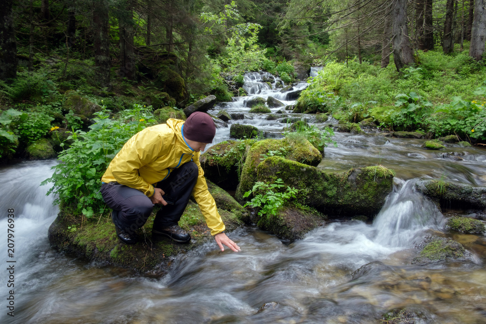 Man drink water from clear mountain stream in the lush forest