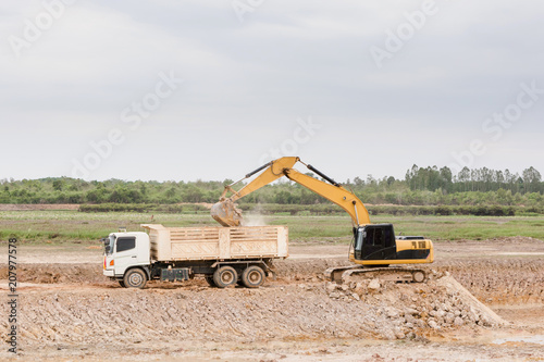 Yellow excavator machine loading soil into a dump truck at construction site