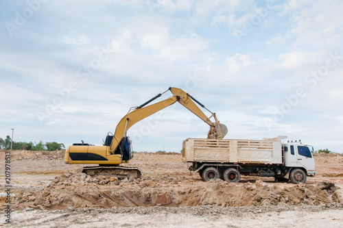 Yellow excavator machine loading soil into a dump truck at construction site