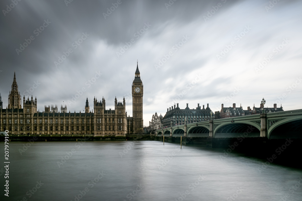 Panoramic long exposure of The Houses of Parliament, the Big Ben and Westminster Bridge in London silhouetted against  thick dark clouds