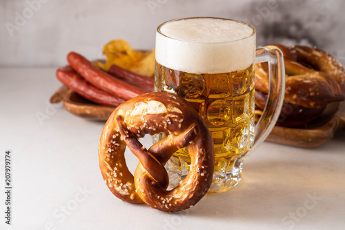 Freshly baked homemade soft pretzel with salt on white table with glass of beer.