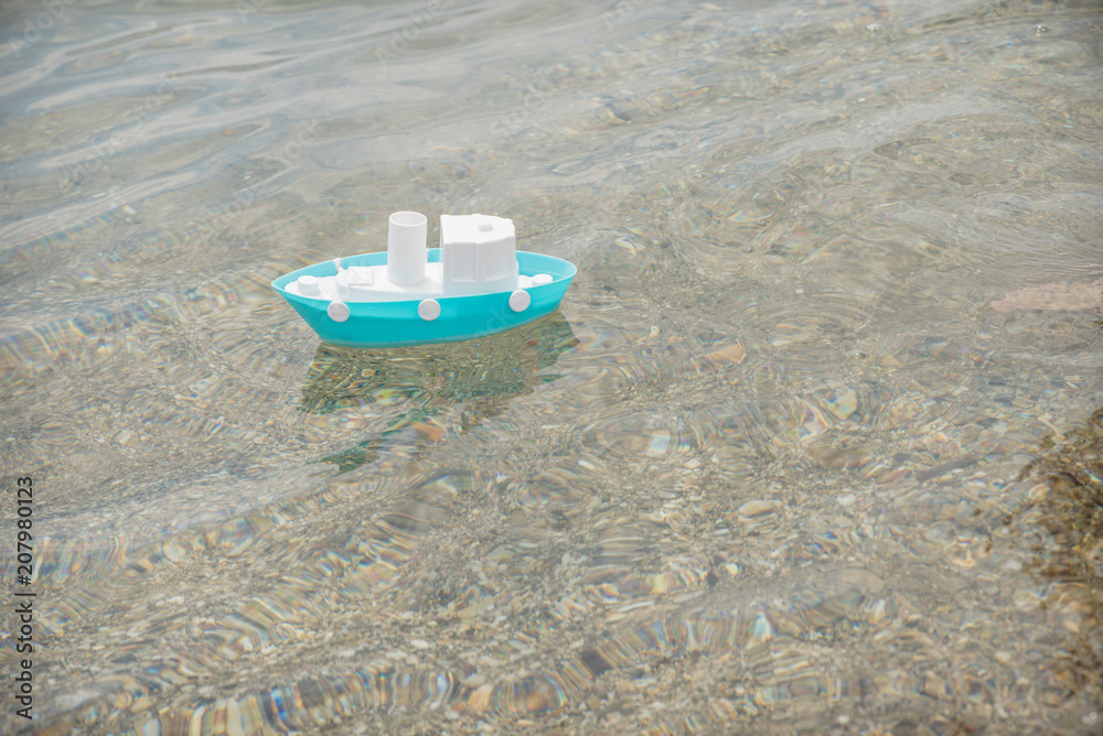 Naklejka premium white and blue toy boat floating on the seashore