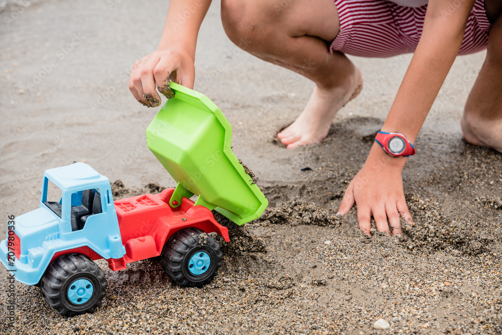 boy playing on the shore of the beach with a green, blue and red toy truck boy playing on the shore of the beach with a green, blue and red toy truck