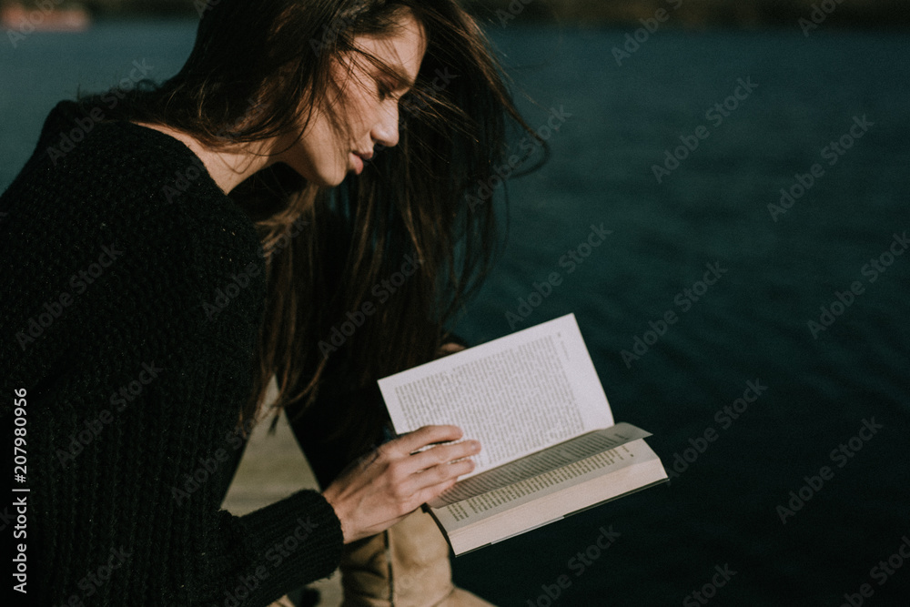 Obraz premium Young woman reading by the seaside