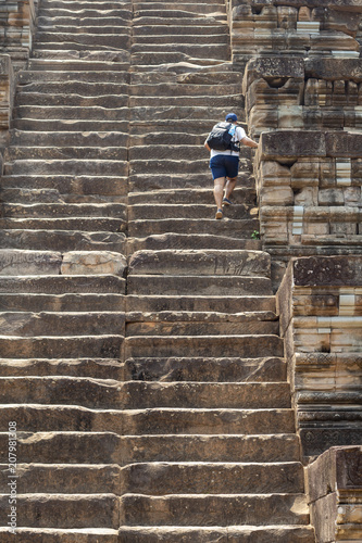 Man tourist climbs the high stair of ancient temple. Endless steps of ancient buddhist temple in Angkor Wat.