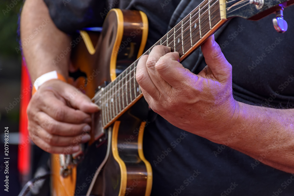 Detail of guitarist's hands and his black electric guitar at an outdoor jazz presentation Detail of guitarist's hands and his black electric guitar at an outdoor jazz presentation