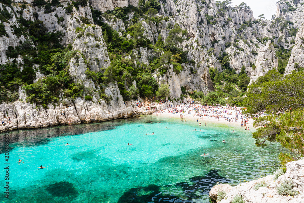 People sunbathing and swimming in the calanque of En-Vau, a natural creek with turquoise water and white sandy beach near Cassis in the french riviera, part of the Calanques National Park.