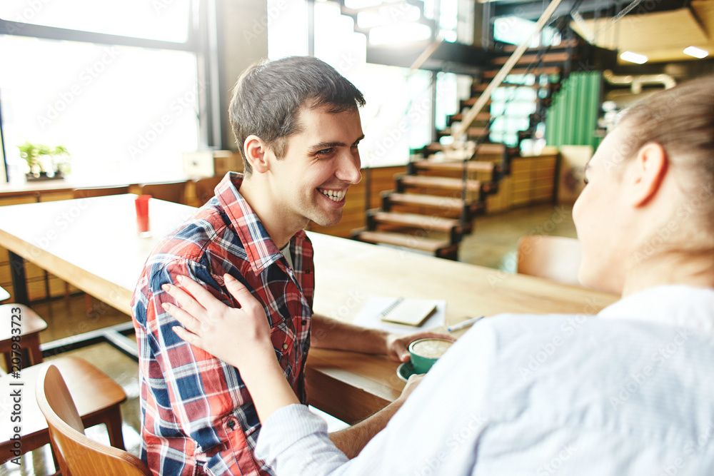 Content laughing man with girl enjoying coffee and conversation chilling at table in modern cafeteria