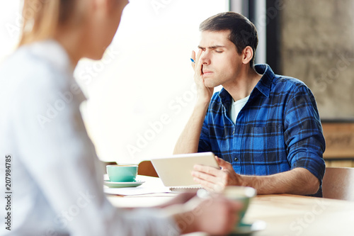 Casual man sitting with studies and tablet in cafeteria rubbing eyes looking tired and overworked.