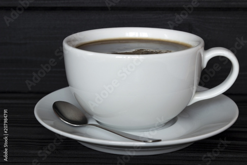 a cup of coffee in a plate with a spoon on a dark wooden background