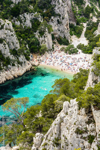 View from above of the calanque of En-Vau, a hard-to-reach narrow natural creek with white sandy beach close to Marseille and Cassis, with people sunbathing and swimming in the crystal clear water. © olrat