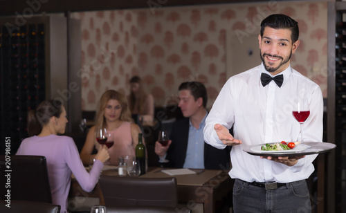 Young waiter with tray welcoming to restaurant