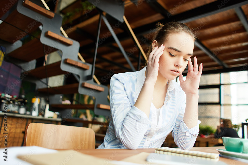 Casual young girl rubbing temples trying to concentrate on subject of studies sitting at desktop Casual young girl rubbing temples trying to concentrate on subject of studies sitting at desktop