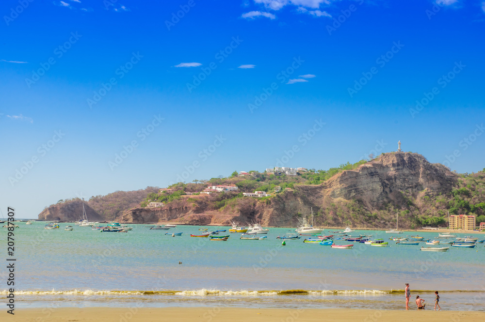 Beautiful outdoor view of some boats in the water with restaurants and hotels on pacific ocean beachfront scene San Juan del sur