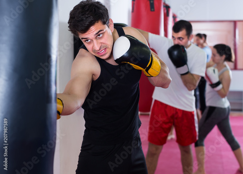 strong sportsman in the boxing hall practicing boxing punches with boxing bag