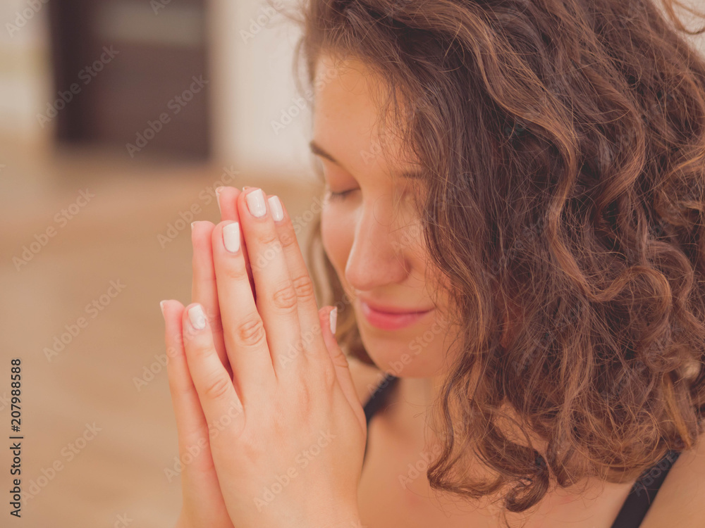 Young beautiful woman with short curly hair meditating in light fitness studio. Hands in namaste. Pray, gratitude, yoga, love God concept. Young beautiful woman with short curly hair meditating in light fitness studio. Hands in namaste. Pray, gratitude, yoga, love God concept.
