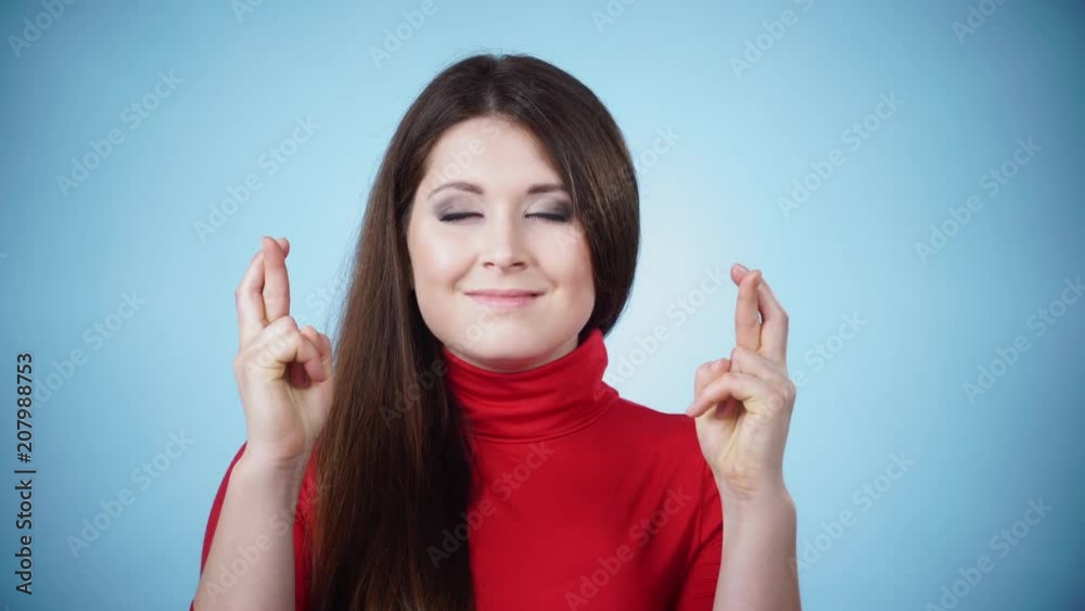 Young woman hopeful eyes closed keeping her fingers crossed hoping, asking for best, good luck, on blue. Human face expressions, emotions 4K Young woman hopeful eyes closed keeping her fingers crossed hoping, asking for best, good luck, on blue. Human face expressions, emotions 4K