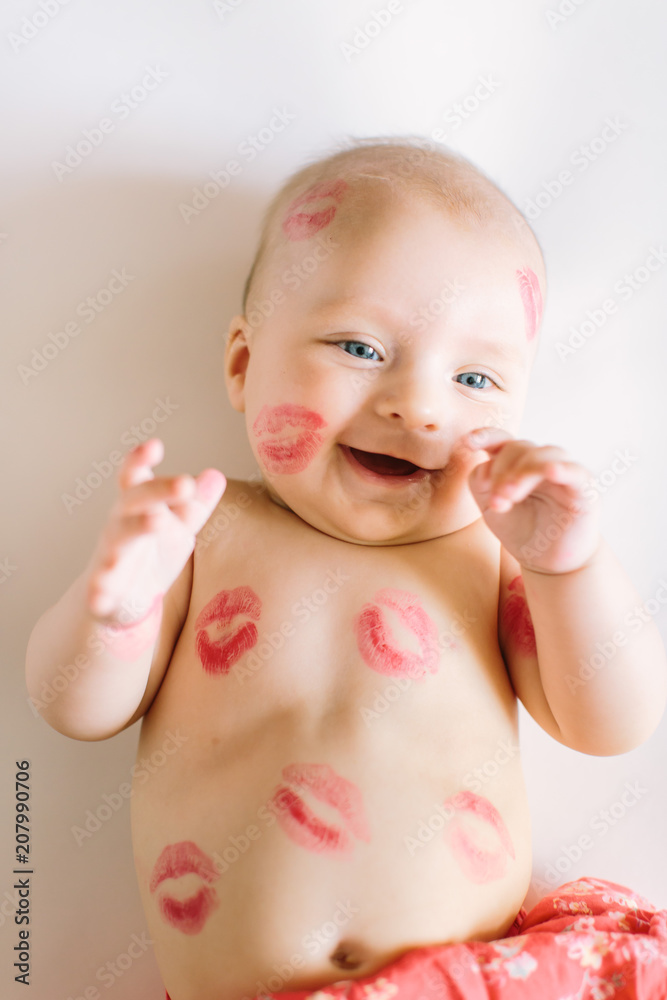 Image of adorable child with red kisses on the skin, happy baby boy sitting down in the studio and isolated on white background, little love angel, romantic holiday, Valentines day concept Image of adorable child with red kisses on the skin, happy baby boy sitting down in the studio and isolated on white background, little love angel, romantic holiday, Valentines day concept