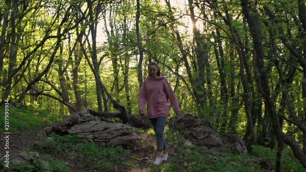 Stunning picture of european young woman in casual clothing strolling through summer forest alone, walking on track among trees slow motion. Human and nature Stunning picture of european young woman in casual clothing strolling through summer forest alone, walking on track among trees slow motion. Human and nature