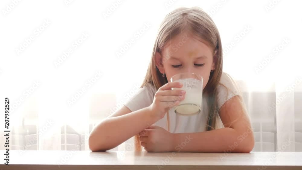 Cute preschool girl drinking fresh milk into glass sitting at the table in the kitchen. Cute preschool girl drinking fresh milk into glass sitting at the table in the kitchen.
