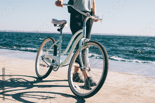 Fototapeta Naklejka Na Ścianę i Meble -  Unrecognizable young woman walking next to her cruiser bicycle