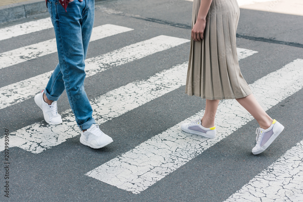 cropped shot of stylish woman in skirt and man in jeans walking on crosswalk at city street cropped shot of stylish woman in skirt and man in jeans walking on crosswalk at city street