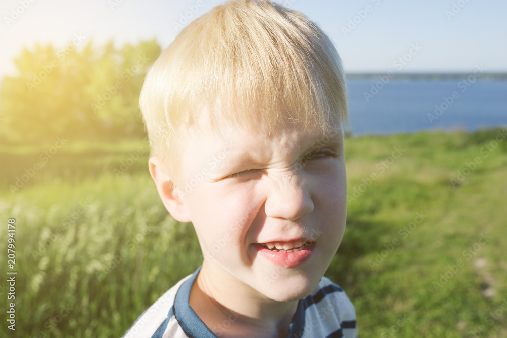 Portrait of blond boy joyful and closing his eye from the sun on nature. Summer activity. Portrait of blond boy joyful and closing his eye from the sun on nature. Summer activity.