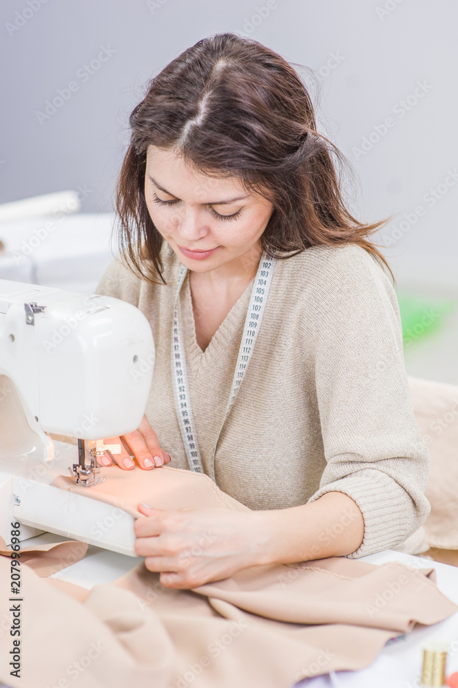 Young woman seamstress sitting and sews on sewing machine. Hobby sewing as a small business concept Young woman seamstress sitting and sews on sewing machine. Hobby sewing as a small business concept