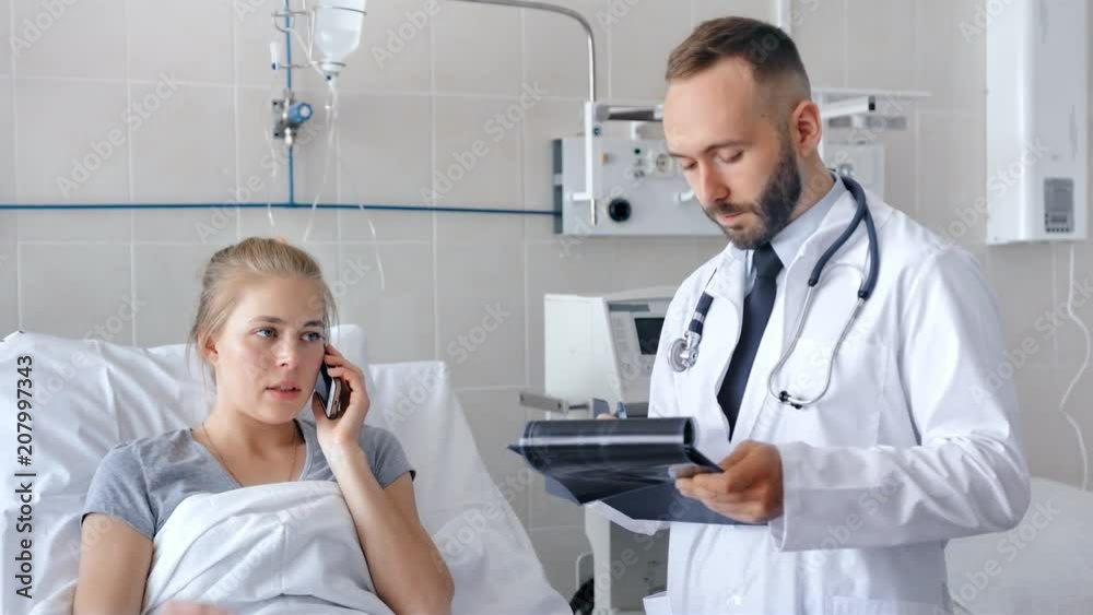 Male doctor visiting female patient in hospital ward. Patient talking on the phone Male doctor visiting female patient in hospital ward. Patient talking on the phone