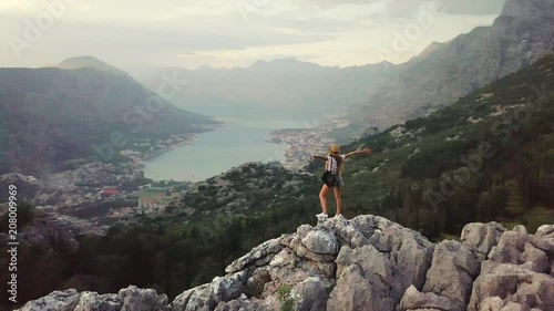 Aerial view of Young traveling woman wearing hat walks on high on the top of the mountain, evening with sunset. Montenegro
