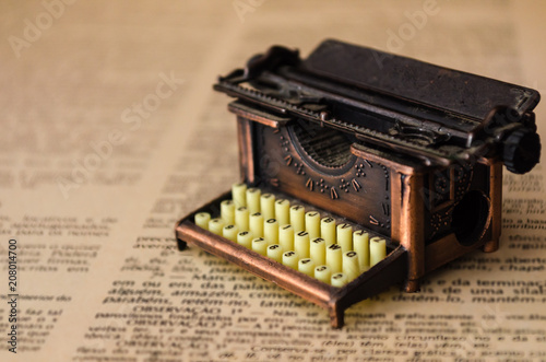 Small typewriter in copper tones in focus on a page of an old book in yellowish tones. Decoration item. Concept of reading  writing  old times  past. Close up. Blurred background.
