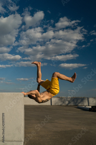 Tricking on street. Martial arts and parkour elements. Man flips back barefoot. Taken from low angle against sky.