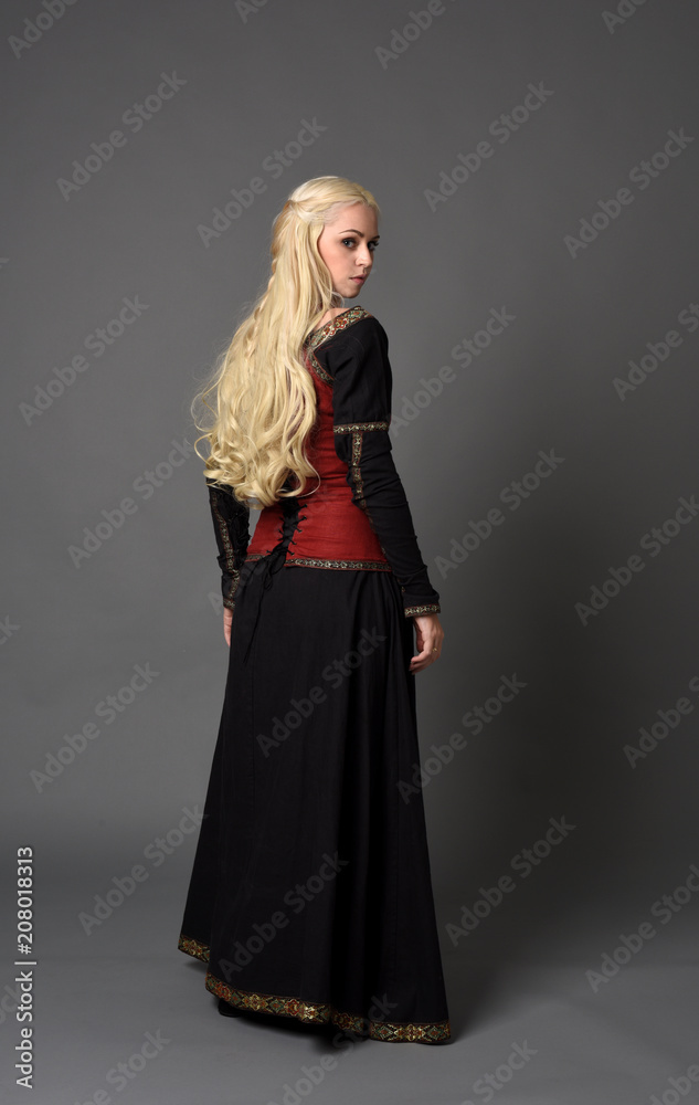 full length portrait of pretty blonde lady wearing a red and black fantasy medieval gown. standing pose on grey background. full length portrait of pretty blonde lady wearing a red and black fantasy medieval gown. standing pose on grey background.