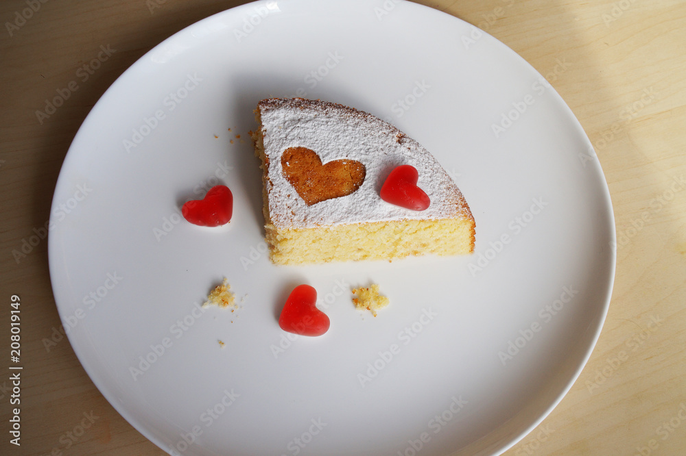 a piece of a festive cake sprinkled with powder and red hearts from marmalade a piece of a festive cake sprinkled with powder and red hearts from marmalade