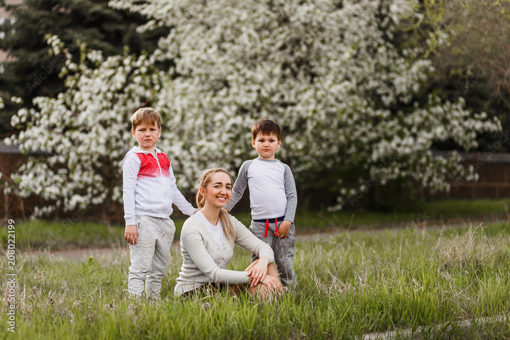 happy mom with two kids sitting on green grass outdoors