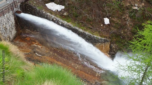 Water discharge from the dam of the Lake Fregabolgia an Alpine artificial lake. Italian Alps. Italy. The water flows rapidly and splashes onto the ground photo