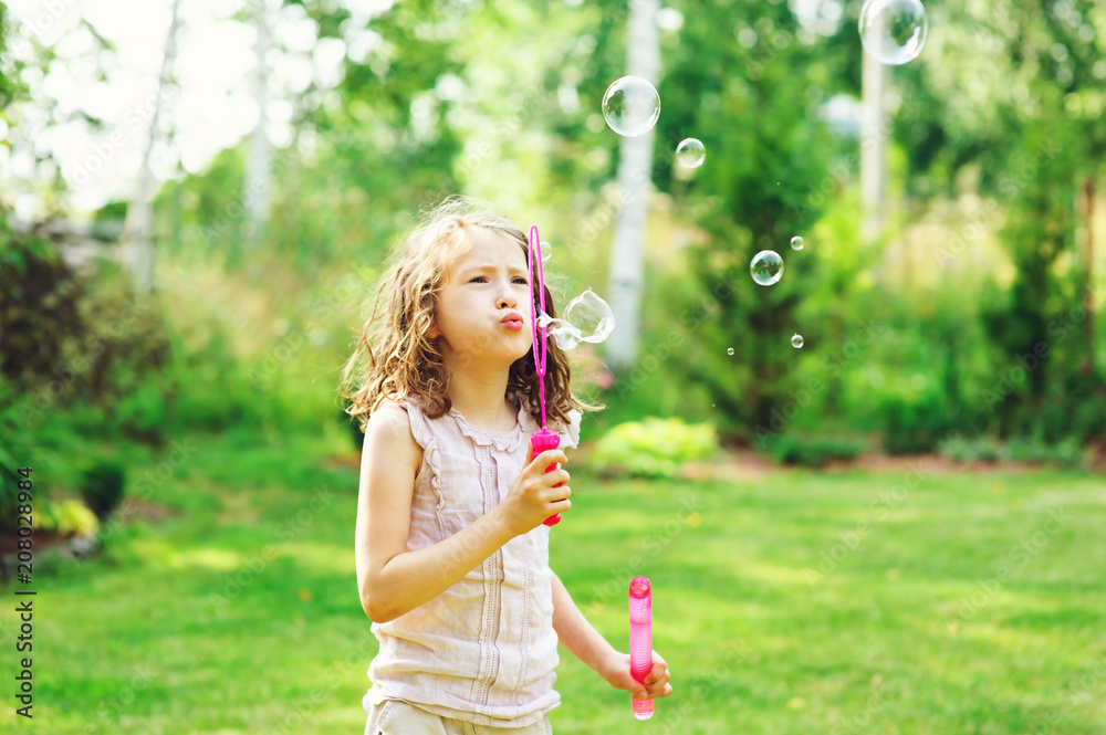 happy kid girl playing with soap bubbles in summer garden