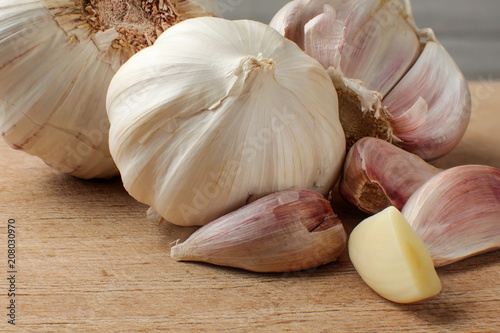 Garlic bulbs and cloves, one of them peeled and cut in half, on old scratched cutting board.