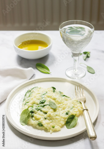Gentle cream risotto with spinach, served with wine. Light background.