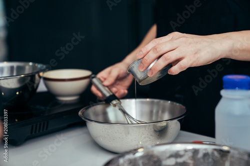 Asian women are mixing the sugar and eggs ingredients of a cake in a stainless bowl in her kitchen for weekend party.