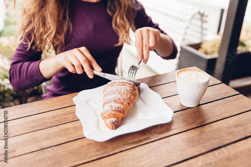 Young woman eating croissant in caffe