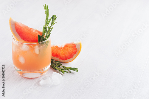 Healthy detox dieting cocktail with grapefruit juice, slice citrus, rosemary and ice cubes on elegance white wooden background.