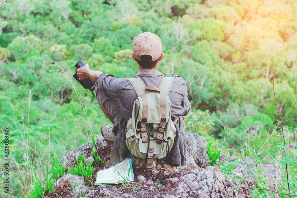 Young man with backpack and holding a binoculars sitting on top of mountain