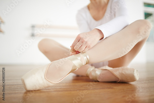 Adult ballerina in white clothes binding ribbon in light studio side view