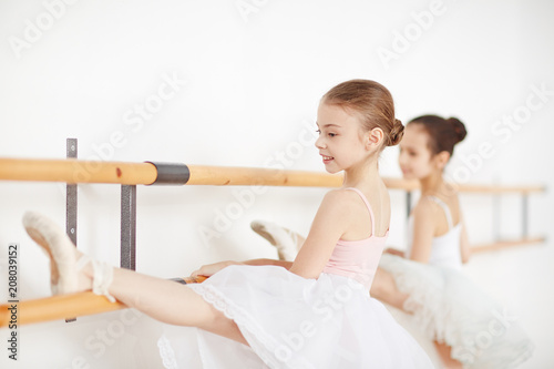 Little ballerinas practicing dances at wooden machine and smiling side view