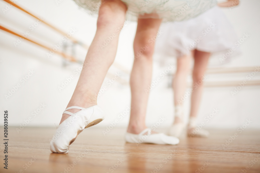 Fototapeta premium Faceless girls leg in ballet shoes making position on parquet with ballerina on background