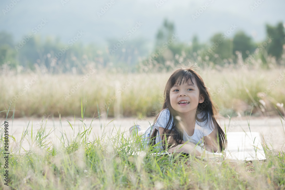 A little girl is lying on her stomach reading on the grass. She has a look of enjoyment on her face and she looks very relaxed. There is quite a bit of negative space around her. A little girl is lying on her stomach reading on the grass. She has a look of enjoyment on her face and she looks very relaxed. There is quite a bit of negative space around her.