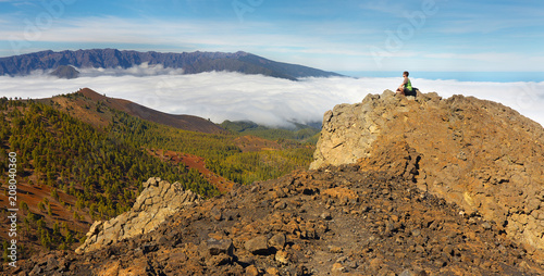Man sitting on the rock watching a volcanic landscape with a Caldera de Taburiente on background, island of La Palma, Canary Islands, Spain