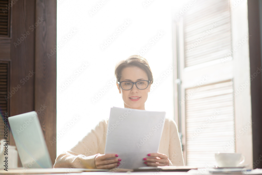 Elegant woman in glasses sitting at cafe table and looking through important documents. Elegant woman in glasses sitting at cafe table and looking through important documents.