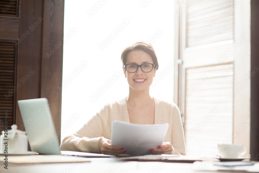 Attractive businesswoman smiling and looking at camera while holding papers in cozy cafe. Attractive businesswoman smiling and looking at camera while holding papers in cozy cafe.